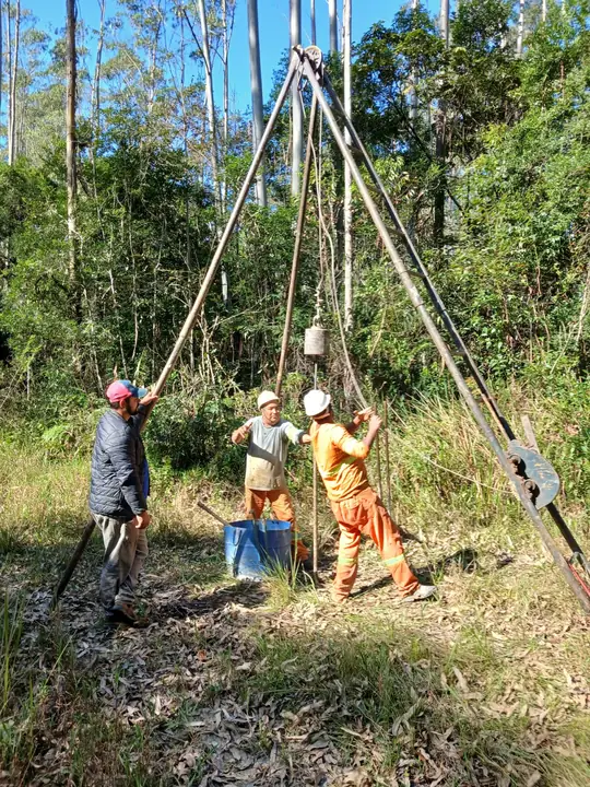 Equipe de sondagem operando o tripé SPT em área com vegetação